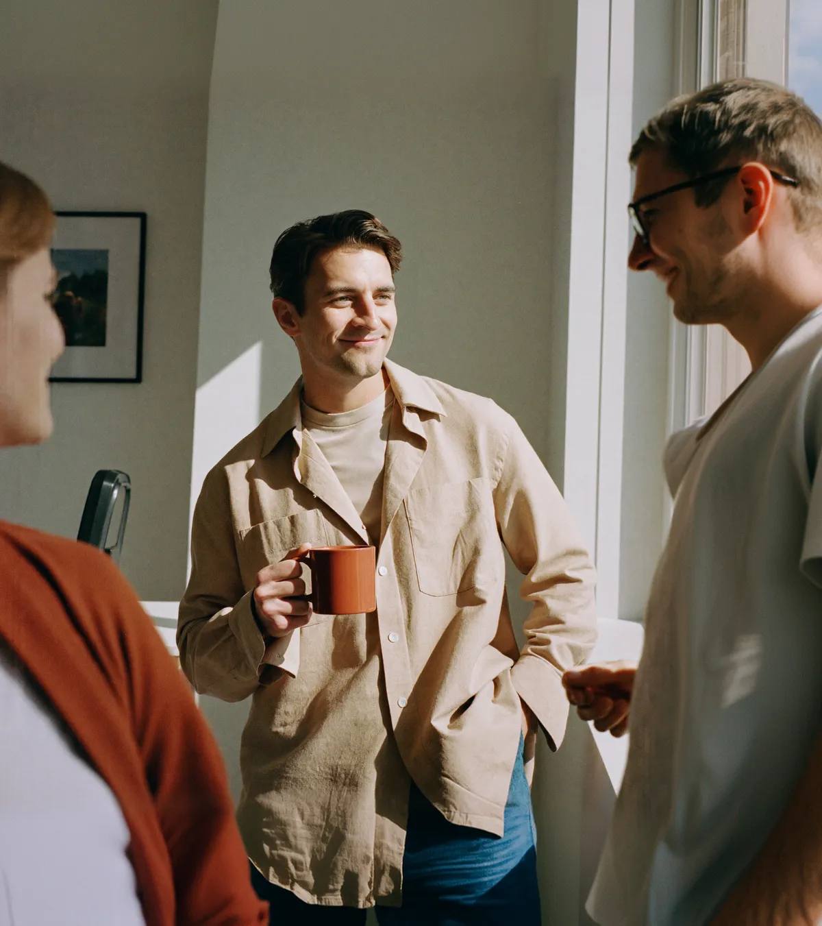 Two people talking in a doorway, holding coffee cups.